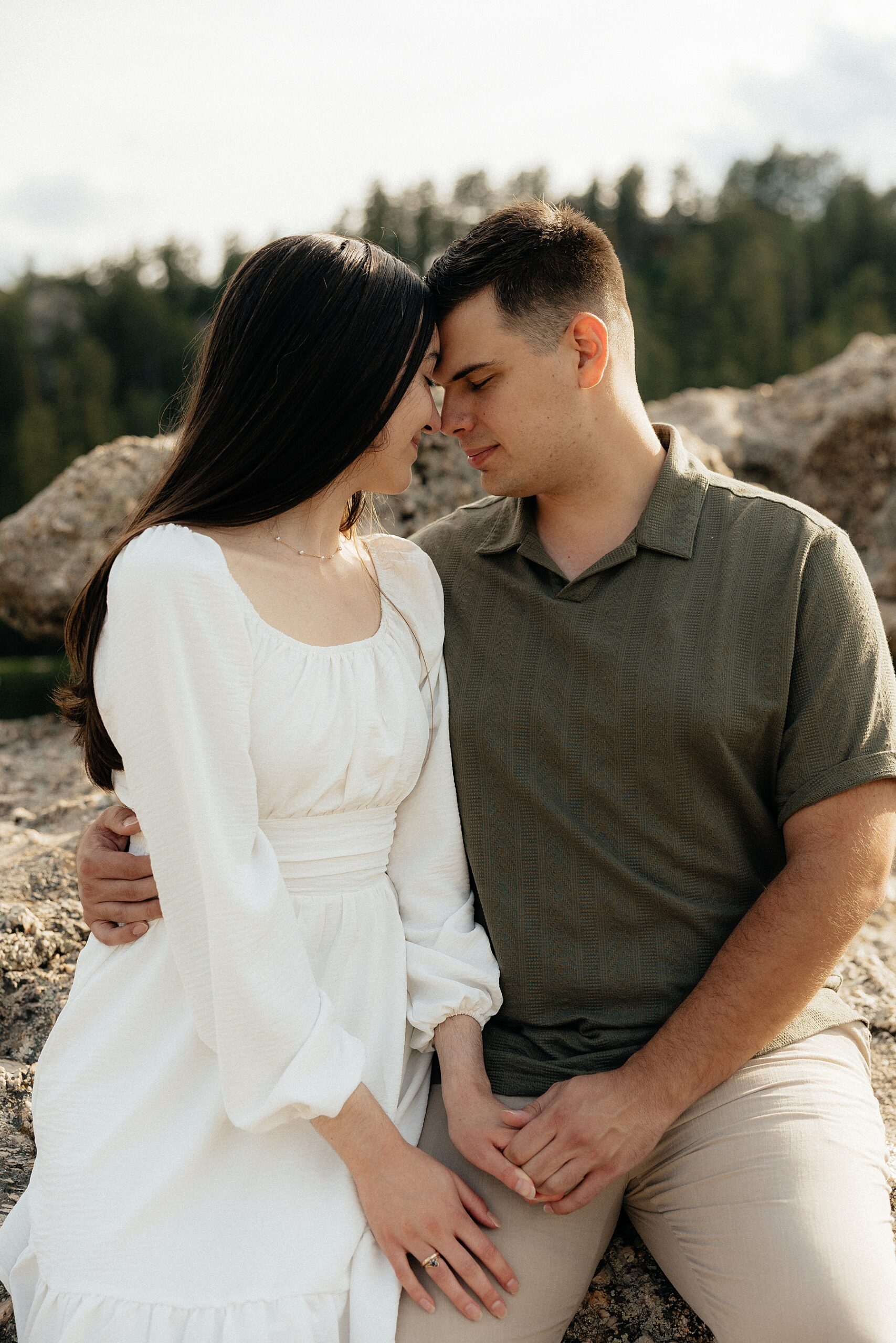 Emily + Harrison forehead to forehead while sitting on a rock.