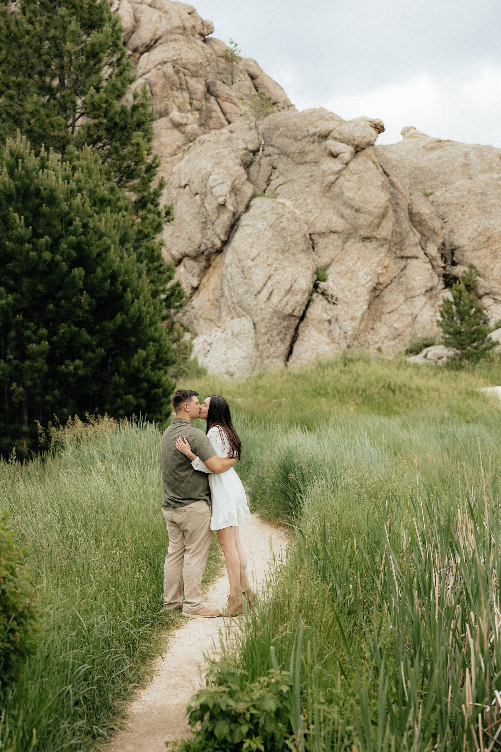 Emily + Harrison kiss while standing on a walking path.