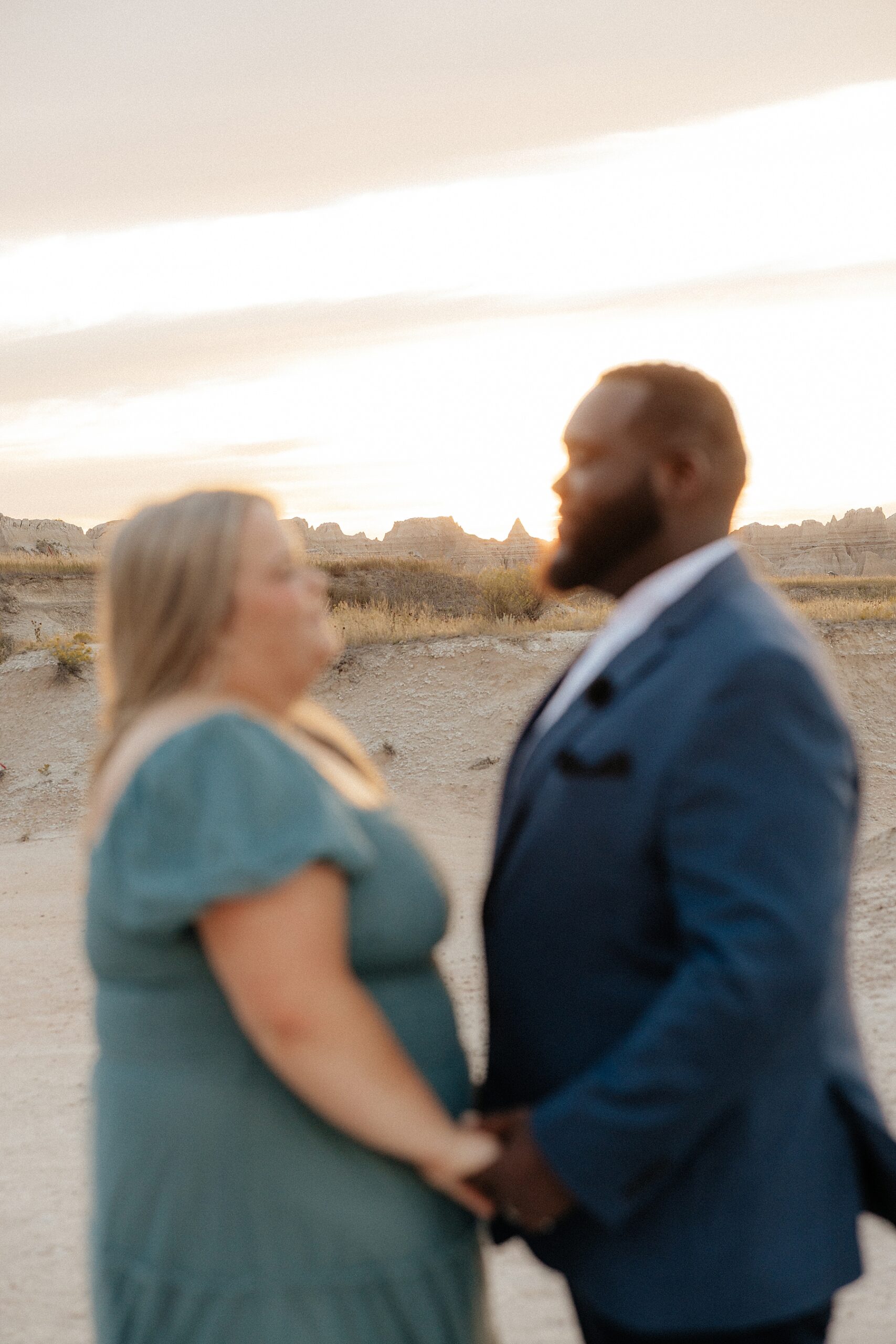 A couple standing hand and hand like they will at their ceremony with the Badlands sunset behind them.