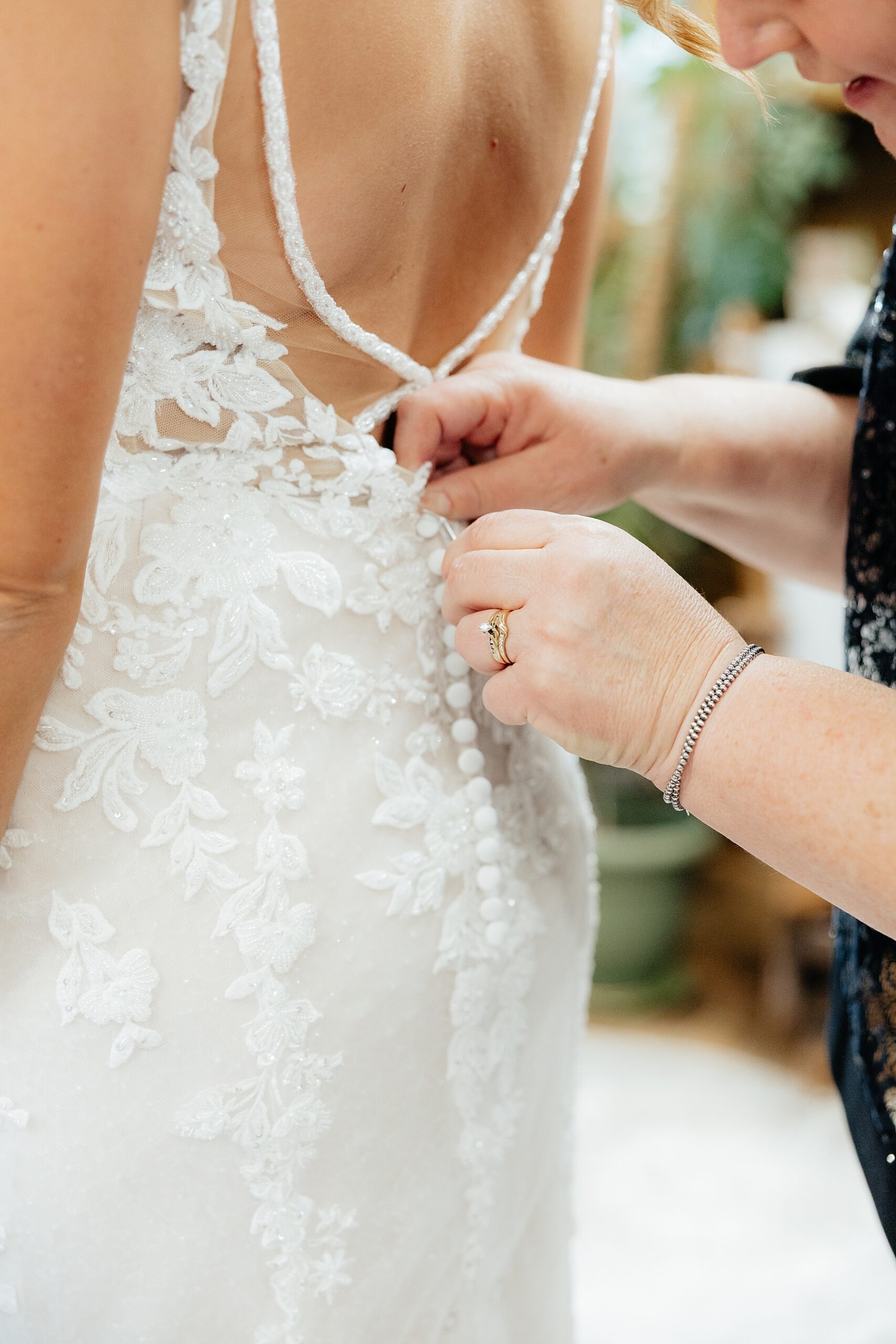 The bride's lace dress being buttoned up.