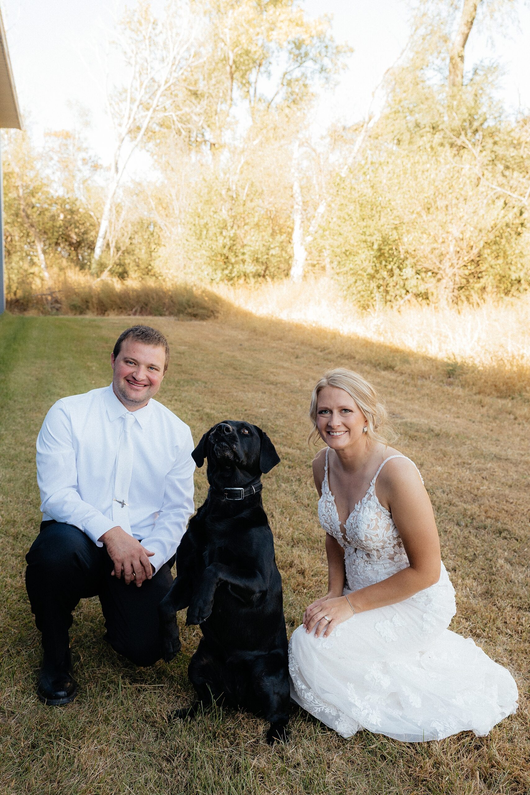The bride and groom next to their dog while she does a trick.