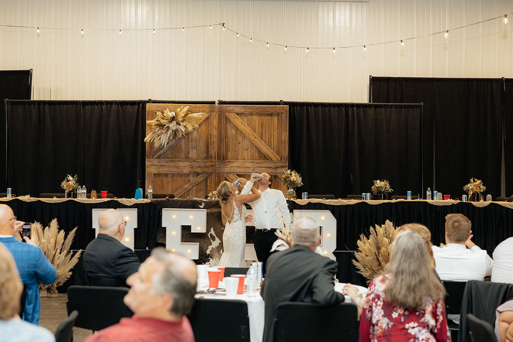 The bride and groom interlacing their arms to drink a beer.