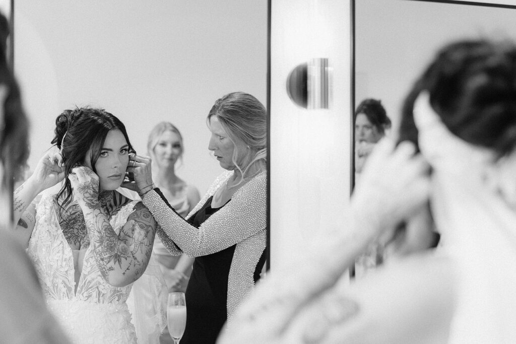 The bride putting in her earrings while looking in the mirror.