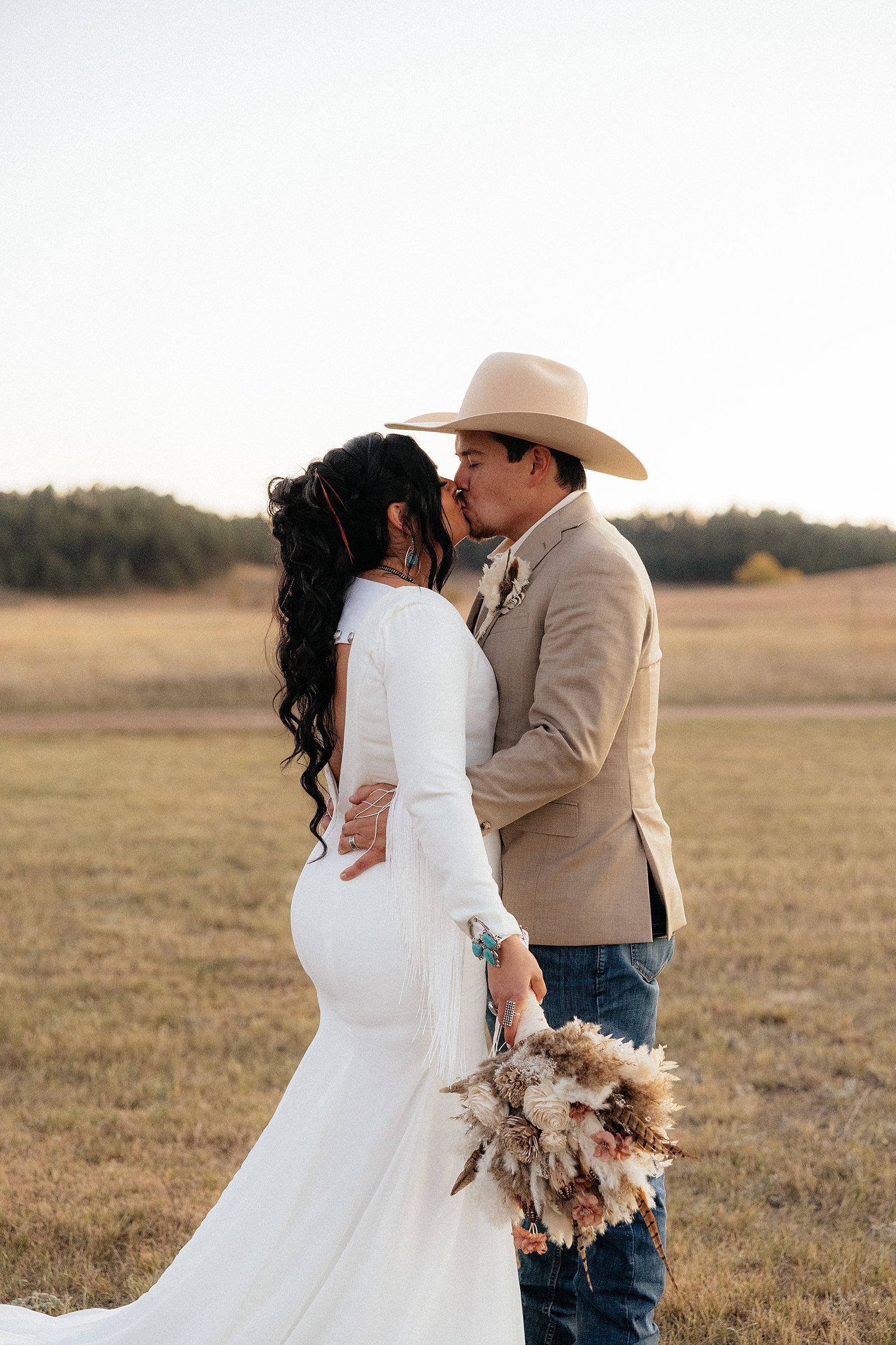 The bride and groom kissing. The bride has a bouquet with pheasant feathers.