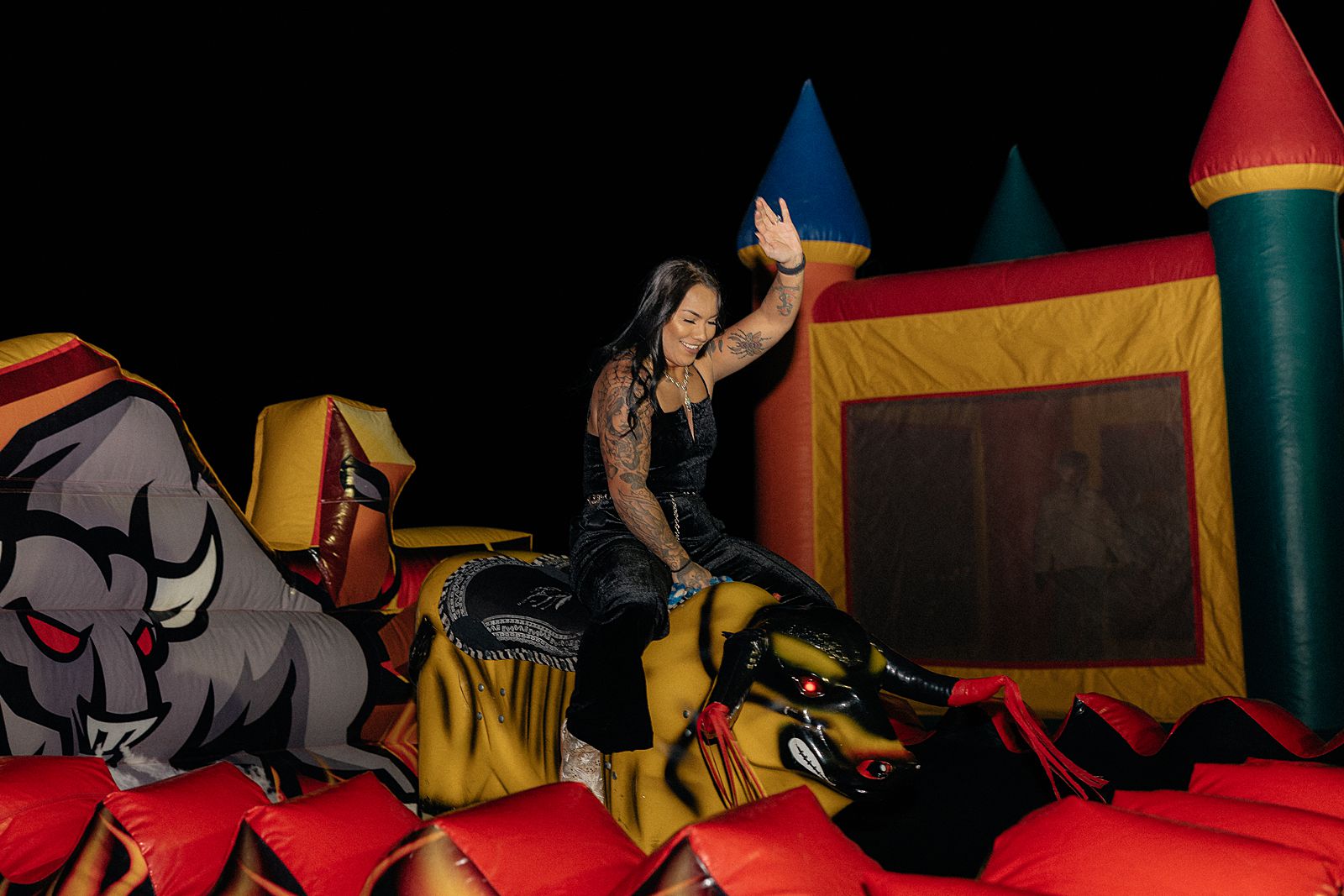 A girl in black riding a mechanical bull.