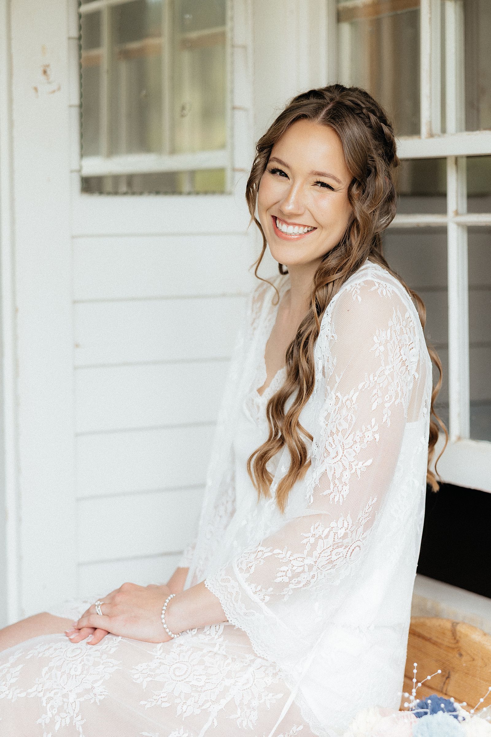 A bride in a lace robe and white pjs smiling at the camera.
