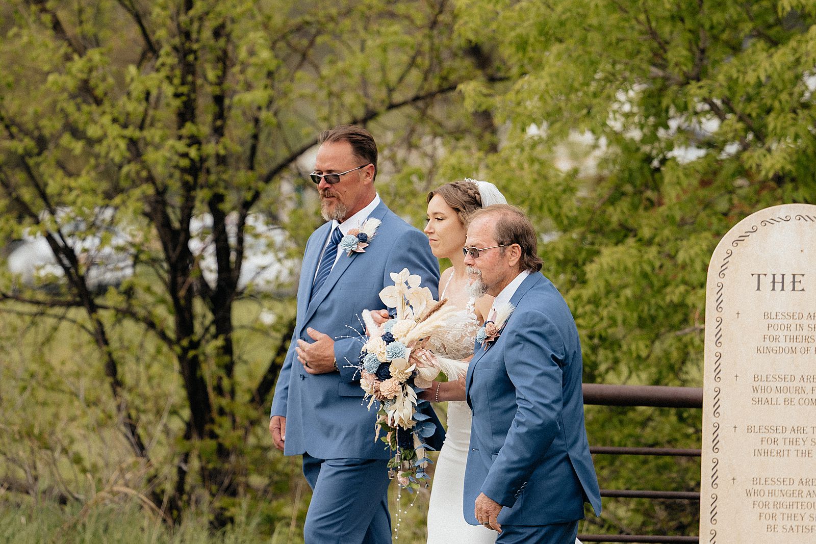 A bride walking down the aisle with her father and step father.