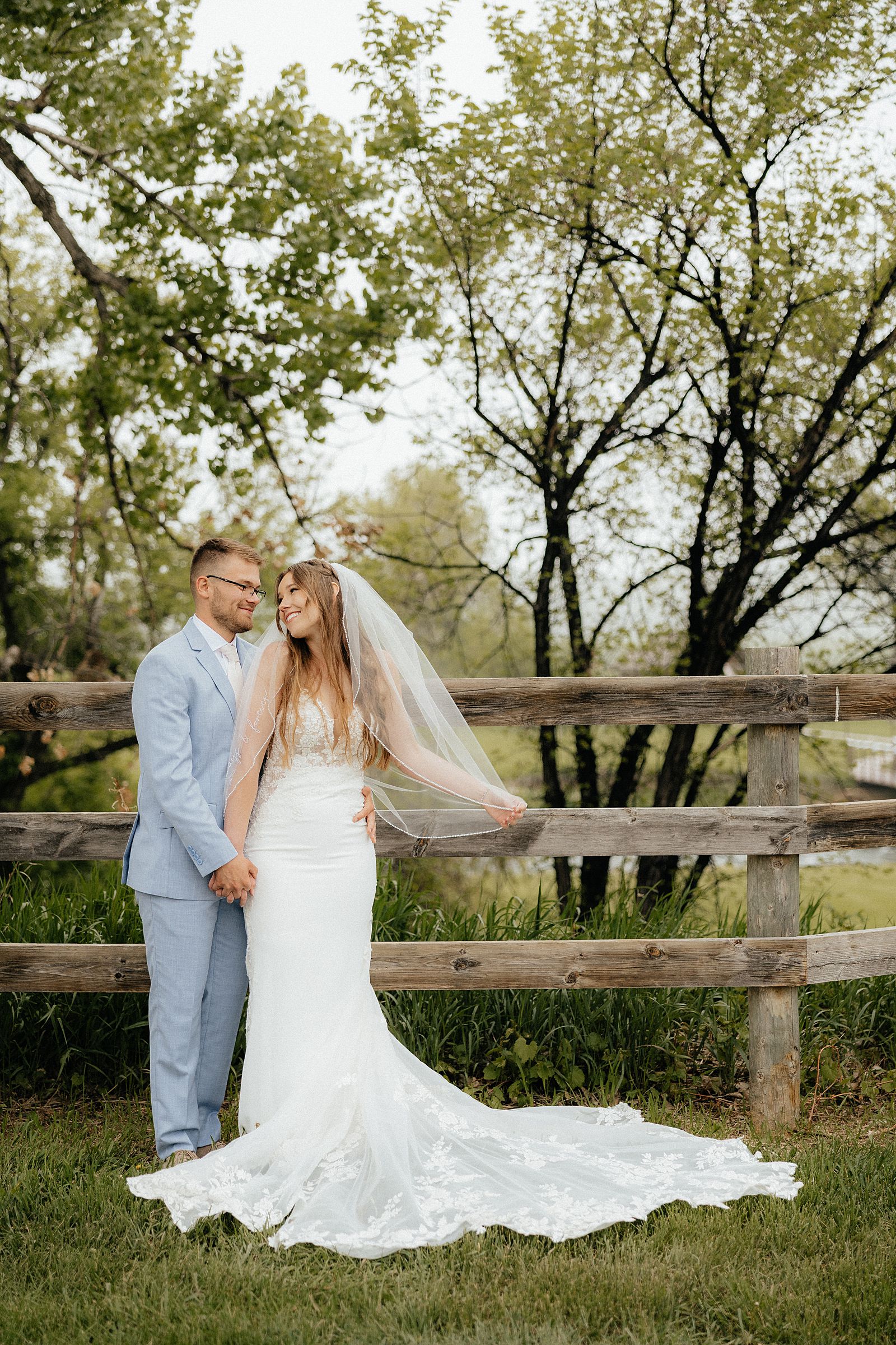 The bride and groom in front of a wooden fence.