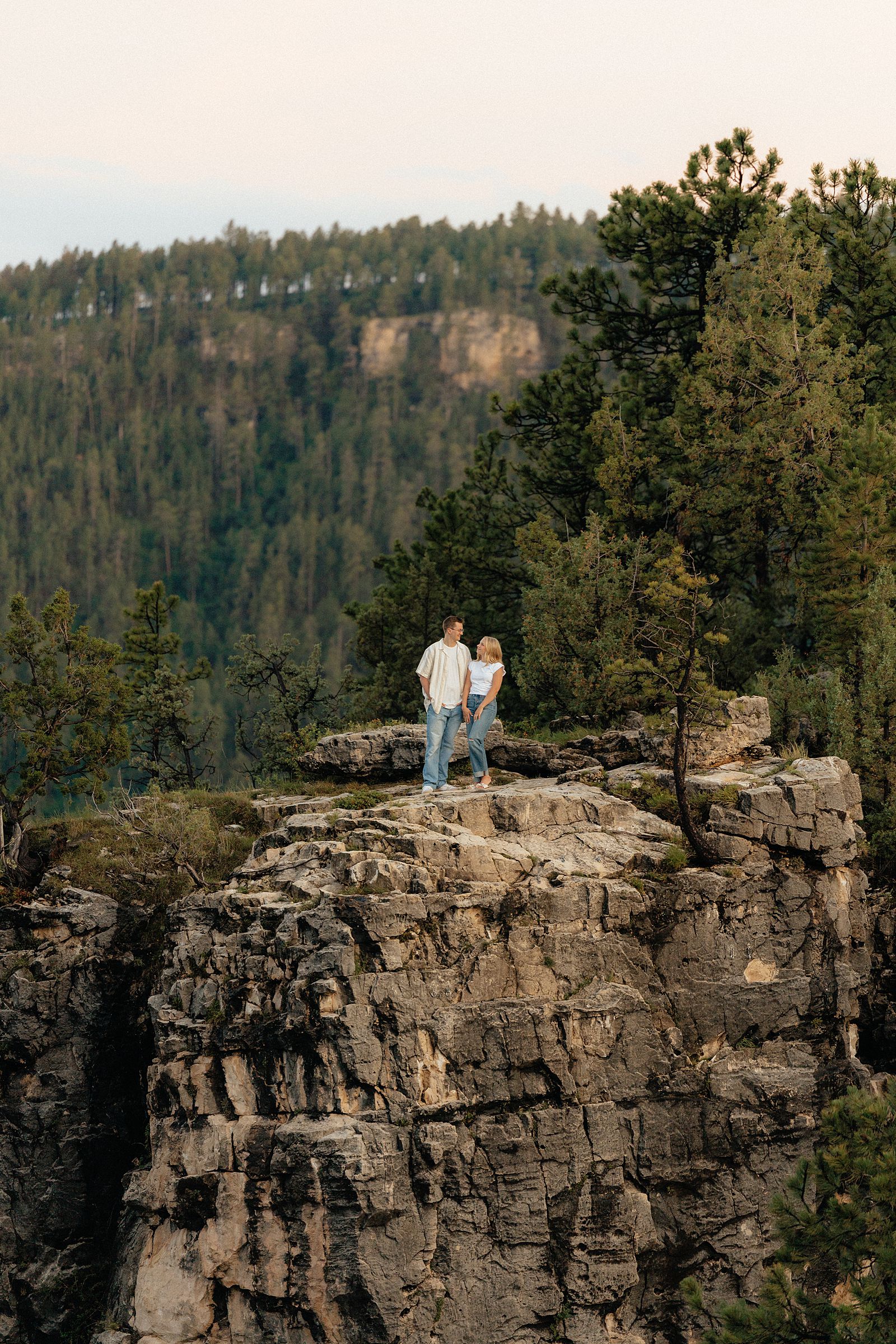 A couple smiling at each other while standing on granite rock formation in the Black Hills.