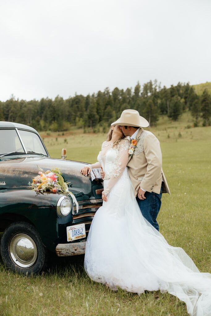 The bride and groom kissing in front of a vintage chevrolet truck.