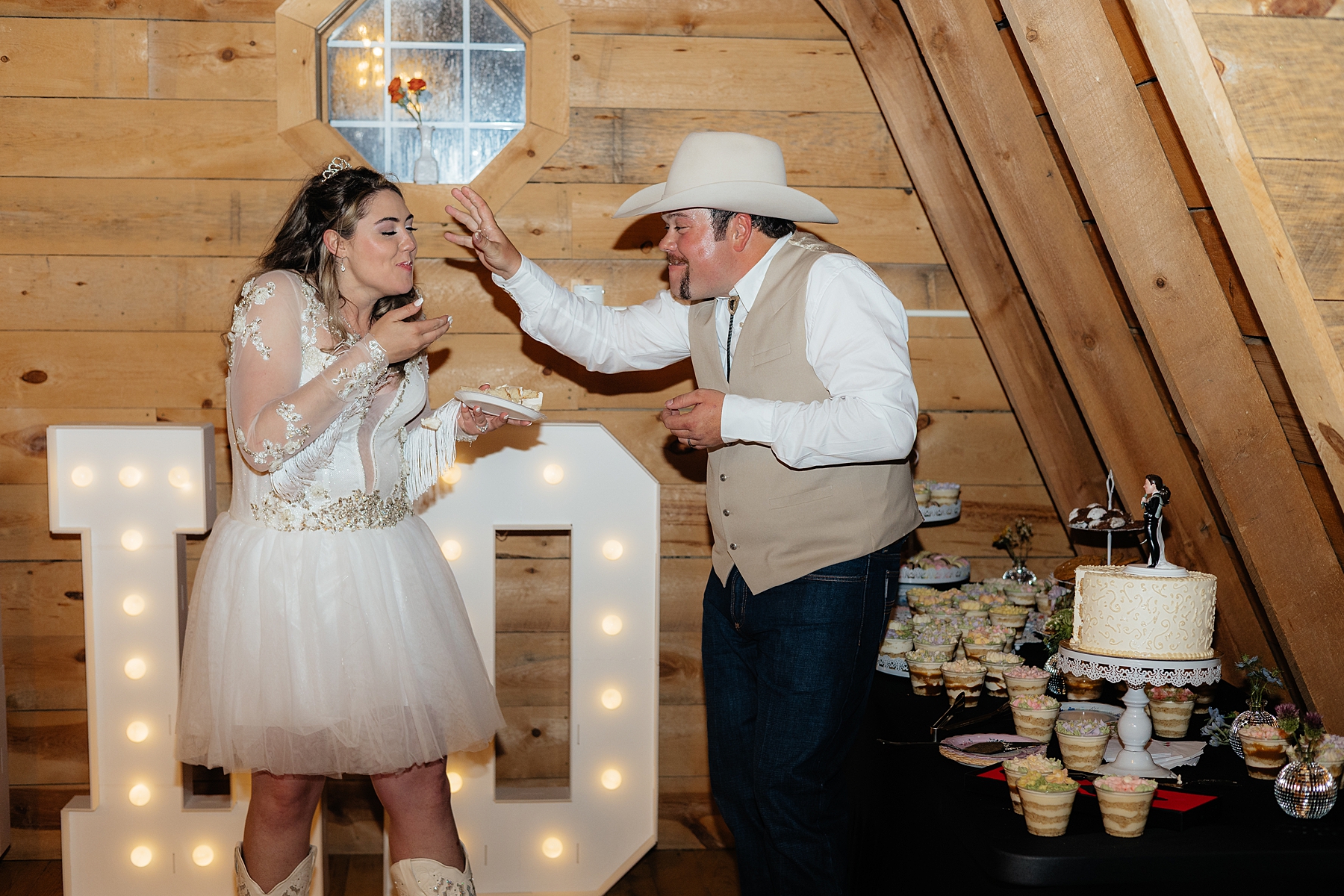 The bride and groom laughing while eating their wedding cake.