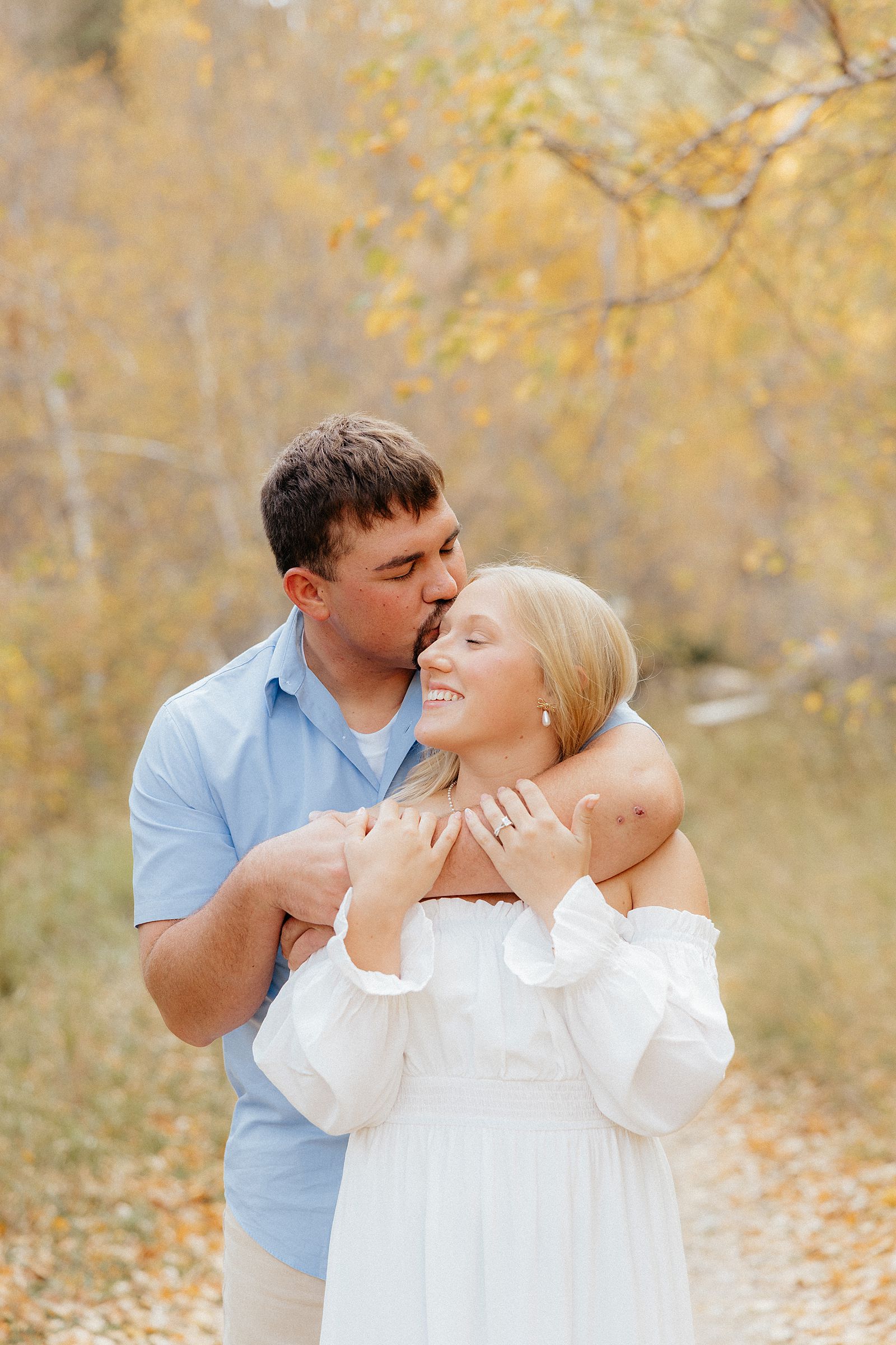 A man kissing his fiance's temple at their fall engagement session.